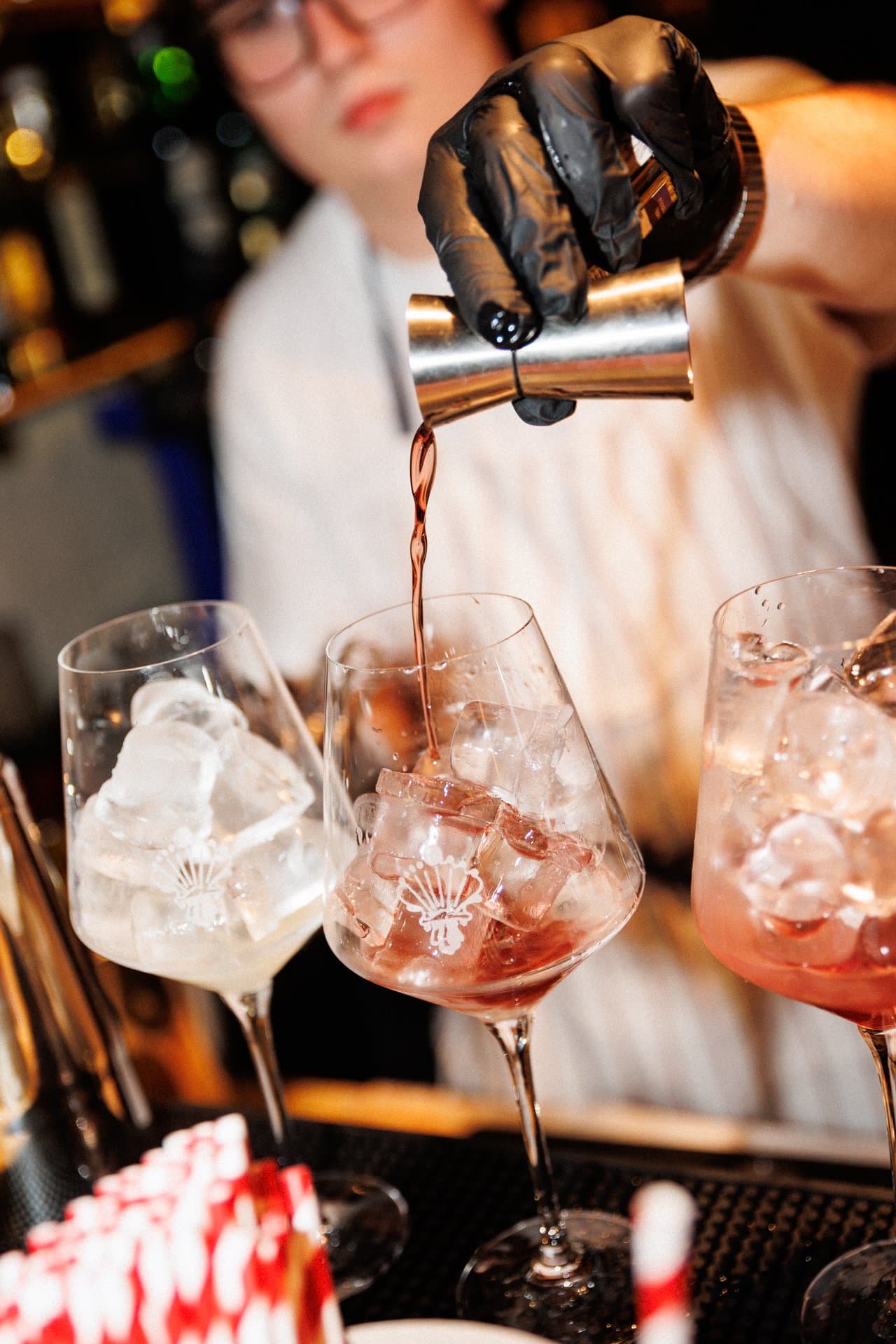 Barman w czarnej rękawiczce nalewa różowy napój do kieliszków z lodem