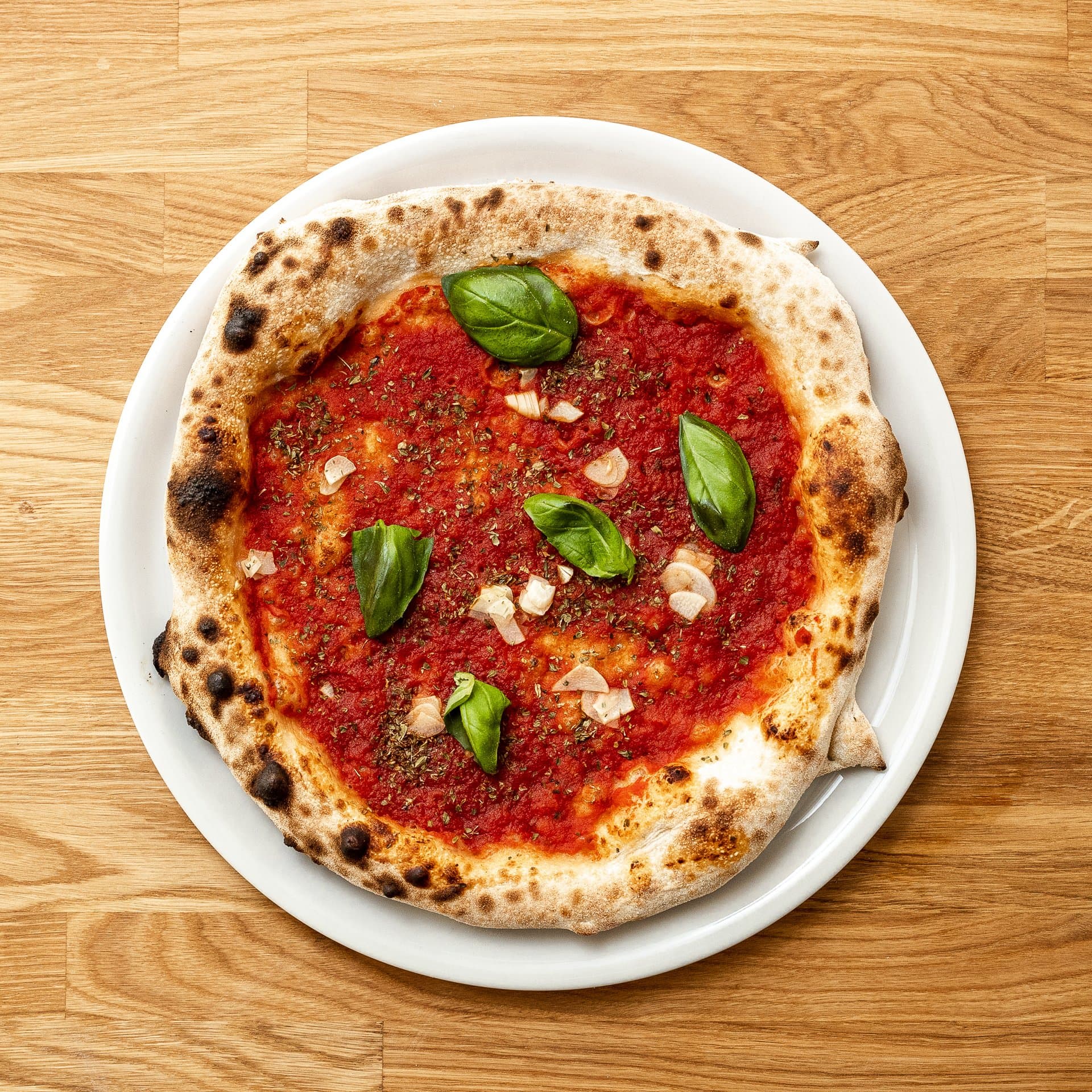 Pizza neapolitańska z bazylią na białym talerzu, widok z góry na drewnianym stole