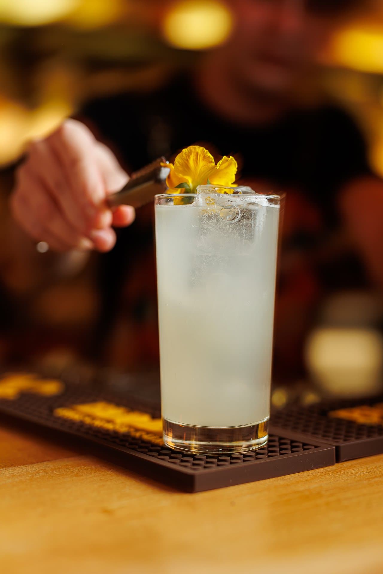 Barman pincetą układa jadalny kwiat na koktajlu w wysokiej szklance