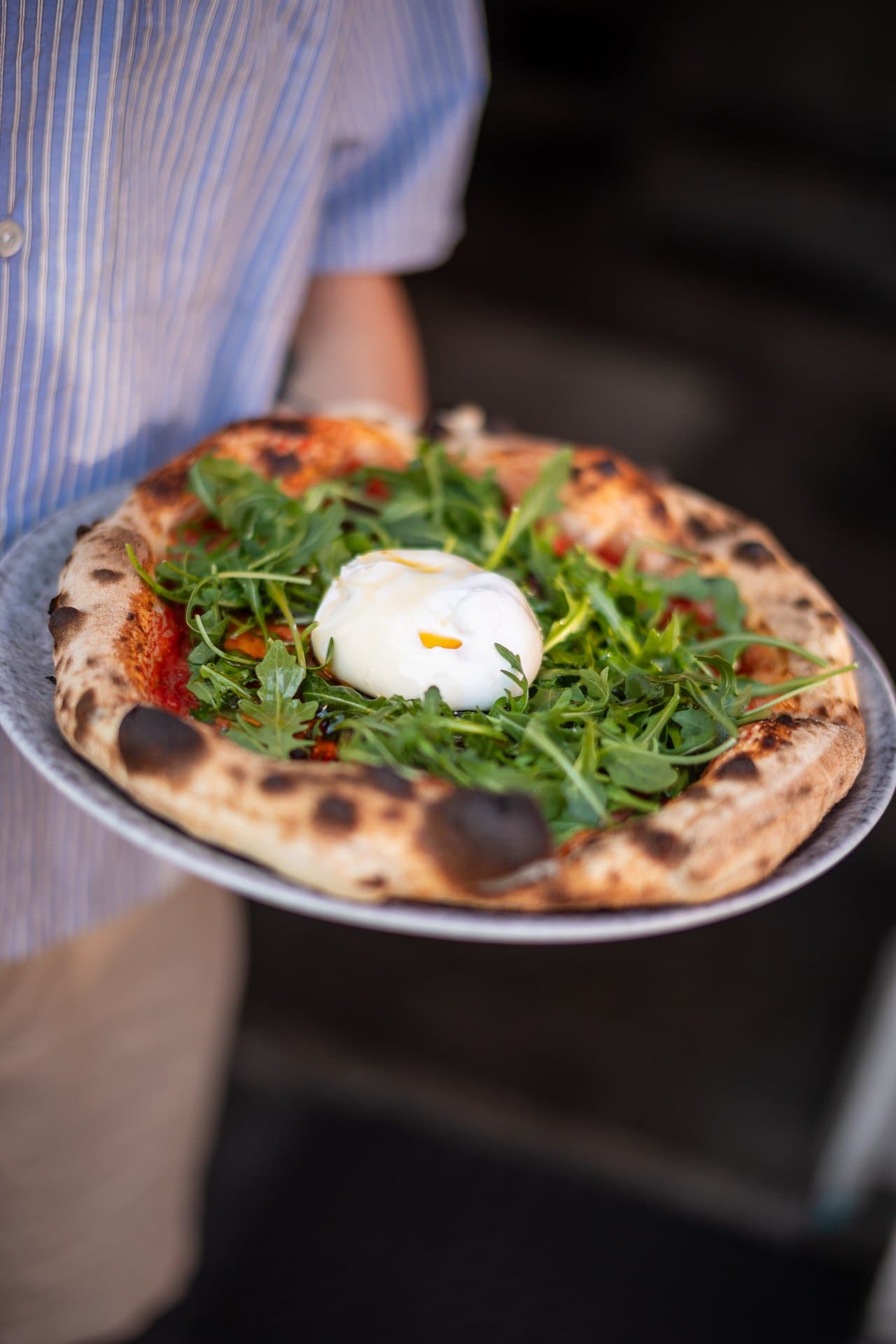 Kelner niesie pizzę z rukolą i burratą na talerzu