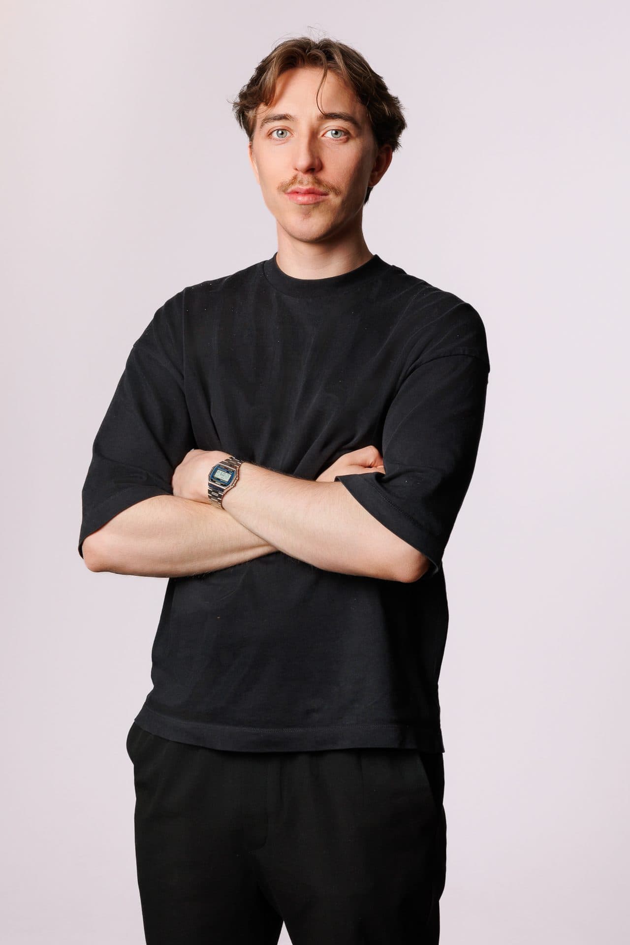 Portret mężczyzny w czarnym T-shircie, ręce skrzyżowane, jasne tło