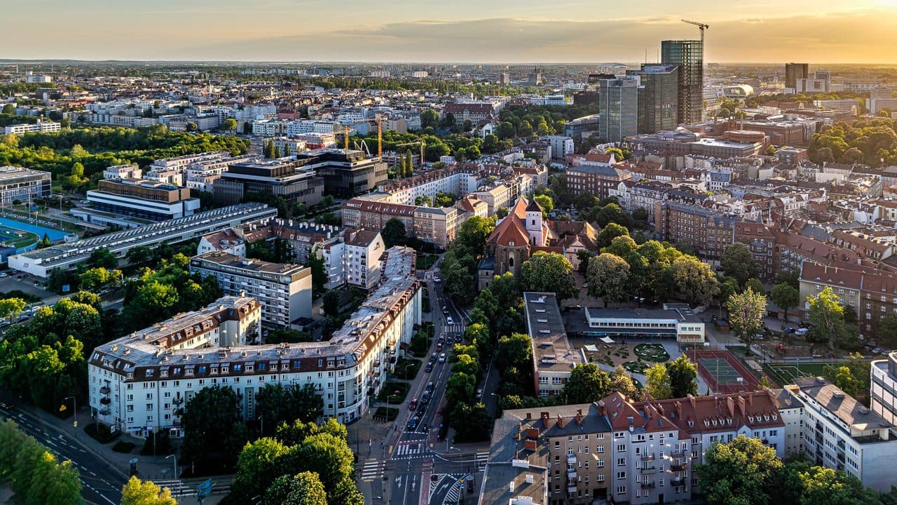 Panorama miasta z drona o zachodzie słońca, kamienice, kościół i wieżowce na horyzoncie