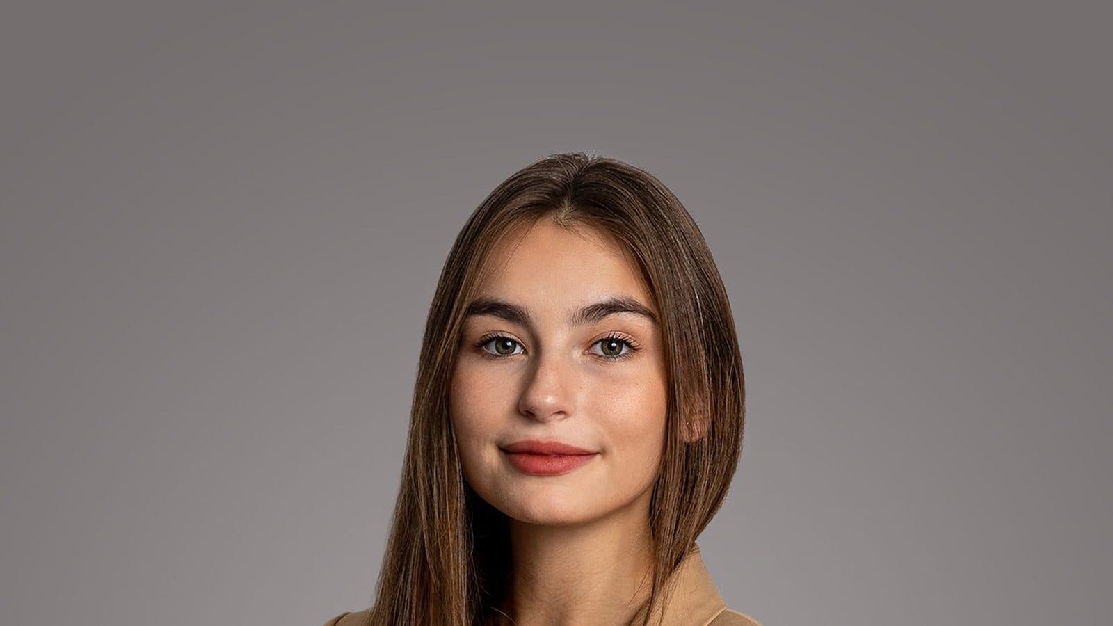 Studyjny portret młodej kobiety w beżowej marynarce na szarym tle, kadr do ramion