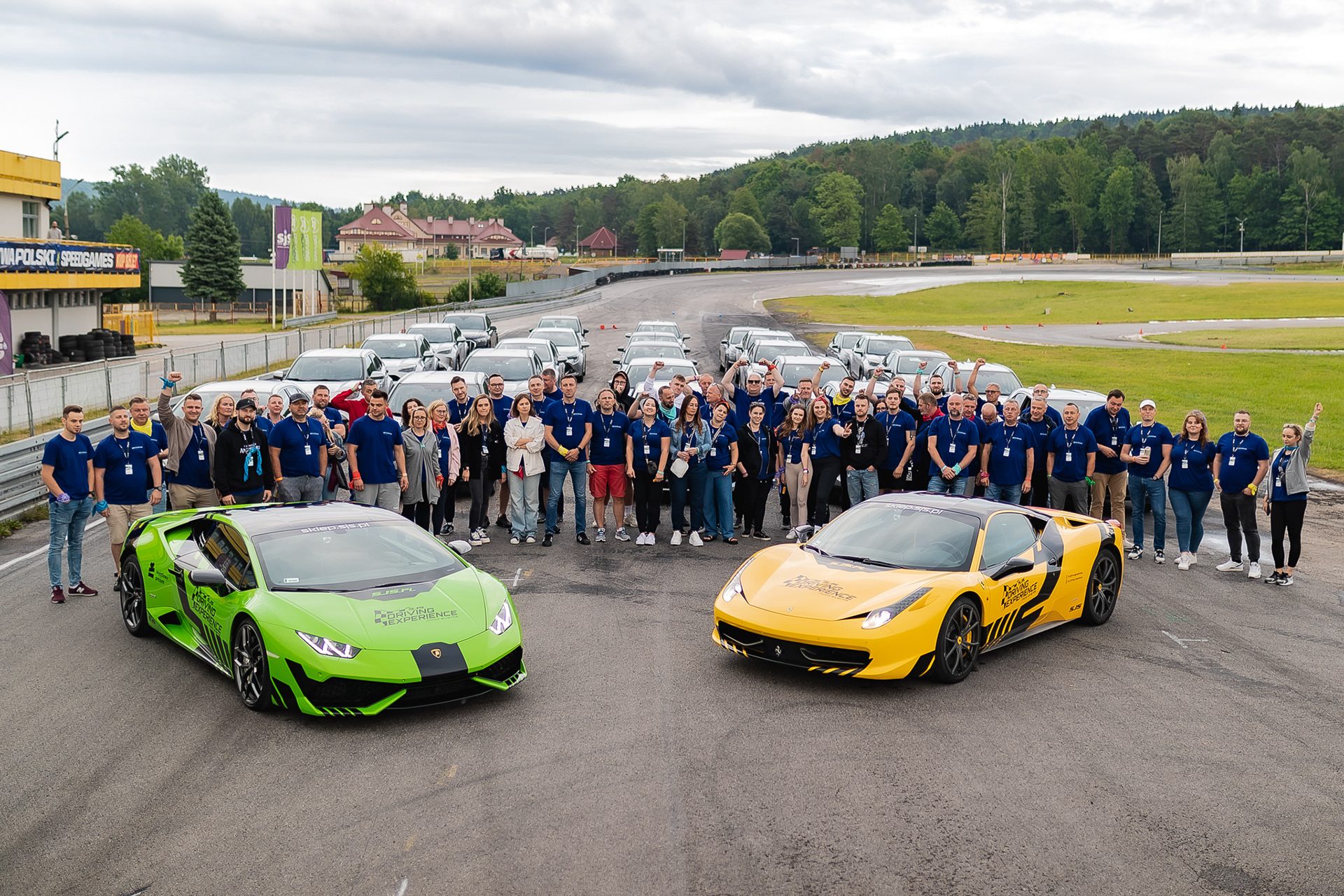 Zdjęcie grupowe uczestników integracji na torze wyścigowym, przed dwoma autami sportowymi